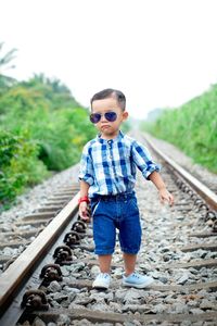 Portrait of little boy walking on railroad tracks against clear sky