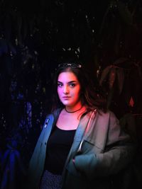 Portrait of beautiful young woman standing against trees at night