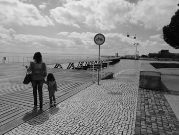 Rear view full length of mother with daughter standing on boardwalk against sky