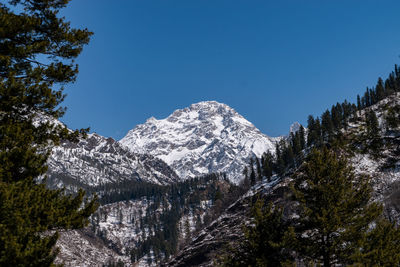 Low angle view of snowcapped mountains against clear blue sky