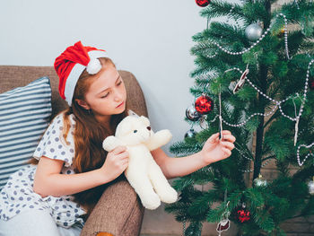 High angle view of girl wearing santa hat while touching christmas tree at home