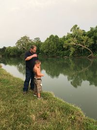 Father and son standing on lake against trees