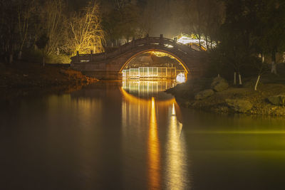 Arch bridge over lake against trees at night