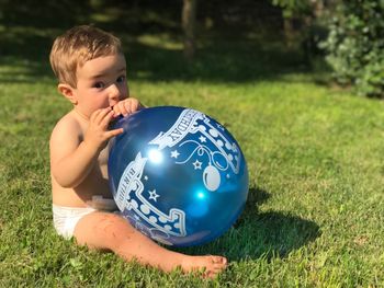 Portrait of baby playing with birthday balloon while sitting on grassy field