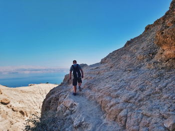 Rear view of man climbing on mountain against clear blue sky