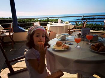 Portrait of girl eating food at table against sea