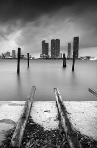 Wooden posts in sea against buildings and cloudy sky in city