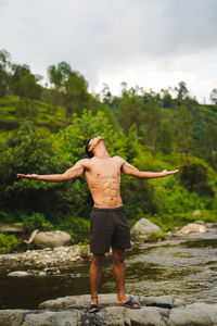 Rear view of shirtless man standing on rock against trees