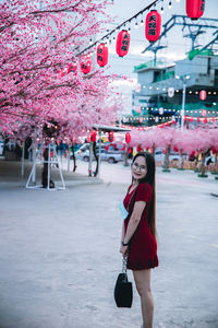 Full length portrait of woman standing by pink flowers in city