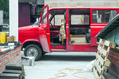 A red old van with open doors for travel and work is parked on a construction site on a summer day