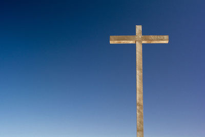 Low angle view of wooden cross against clear blue sky