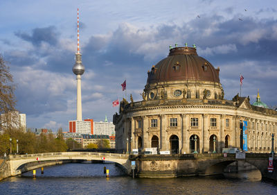 View of built structure by river against cloudy sky