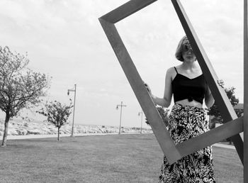 Woman holding picture frame on land against sky