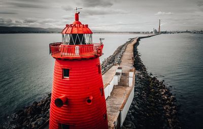 Red lighthouse by sea against sky