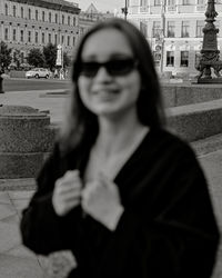 Portrait of young woman standing against buildings in city