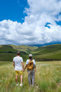 Rear view of people walking on field against sky