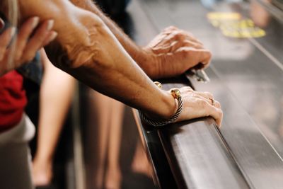 Cropped hands of people by railing of escalator
