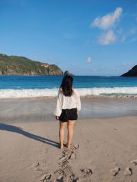 Rear view of woman on beach against sky