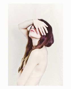 Side view of naked young woman covering face against white background