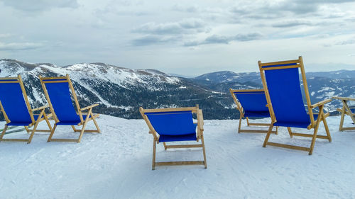 Deck chairs on snow covered mountain against sky