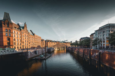 Bridge over river amidst buildings in city against sky