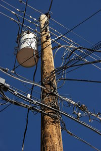 Low angle view of electricity pylon against blue sky