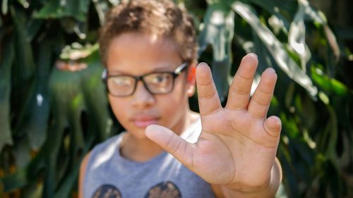 Portrait of boy wearing eyeglasses while gesturing against plants