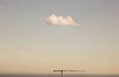 Distant view of crane against sky at construction site during sunset