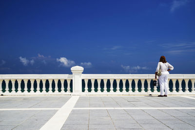 Rear view of woman standing by railing against sky