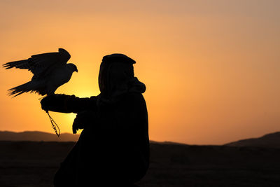 Silhouette woman with arms outstretched standing at sunset