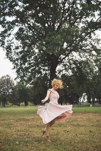 Woman in dress walking on field against trees