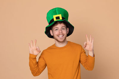 Smiling man wearing green hat standing against beige background