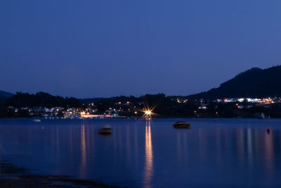 Illuminated city by sea against clear sky at night