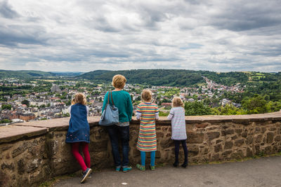 Full length of mother with children standing at observation point against cloudy sky