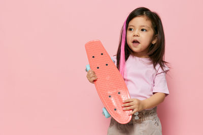 Portrait of smiling young woman holding tape measure against pink background