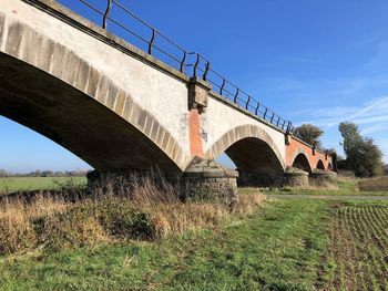 Low angle view of arch bridge on field against sky