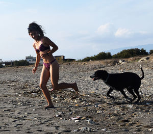 Young woman with dog standing on beach against sky