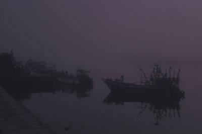 Silhouette boats in sea against sky at dusk