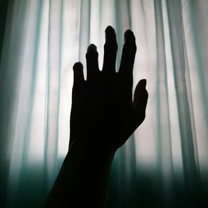 Cropped image of silhouette hand by curtain
