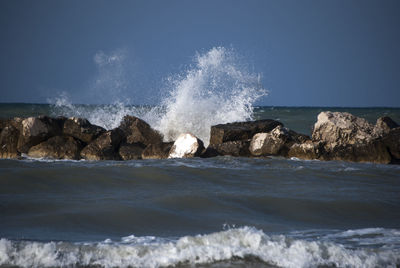 Waves splashing on rocks against sky