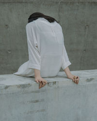 Rear view of young woman sitting on retaining wall