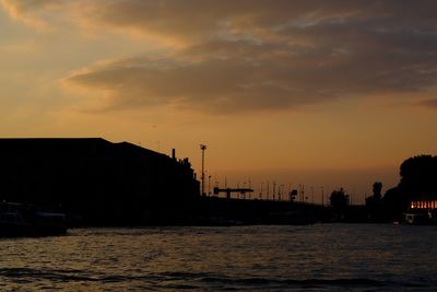 Silhouette buildings by sea against sky during sunset