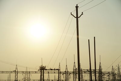 Low angle view of silhouette electricity pylons against sky during sunset