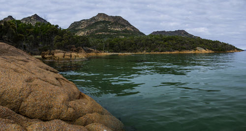 Scenic view of sea by mountain against sky