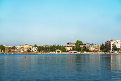 Sea by buildings in city against clear blue sky