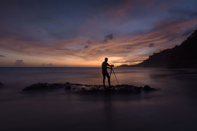 Silhouette man standing on rock against sea during sunset