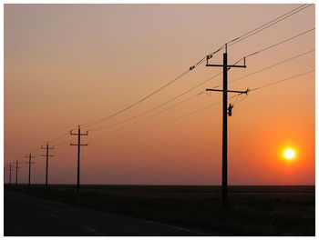 Electricity pylons on field at sunset