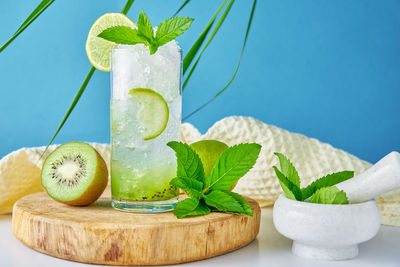 Glass of water with kiwi, lime and mint on blue background