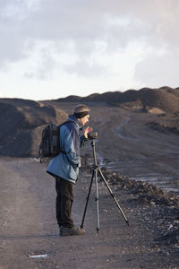 Side view of man photographing while standing against sky