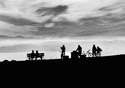 Silhouette people walking on shore against sky